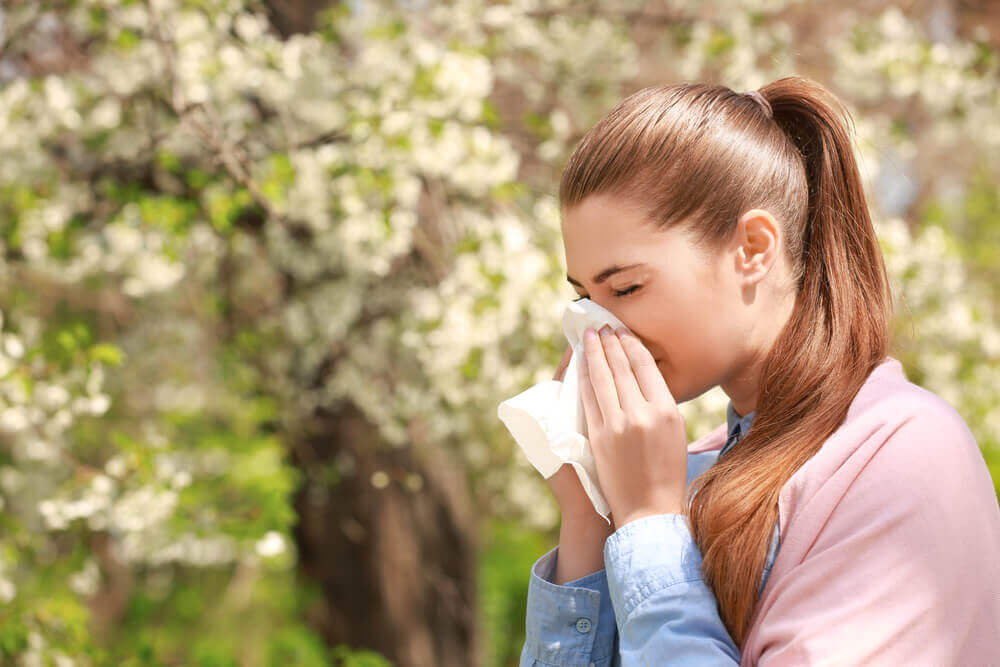 Woman sneezing outdoors among blooming trees