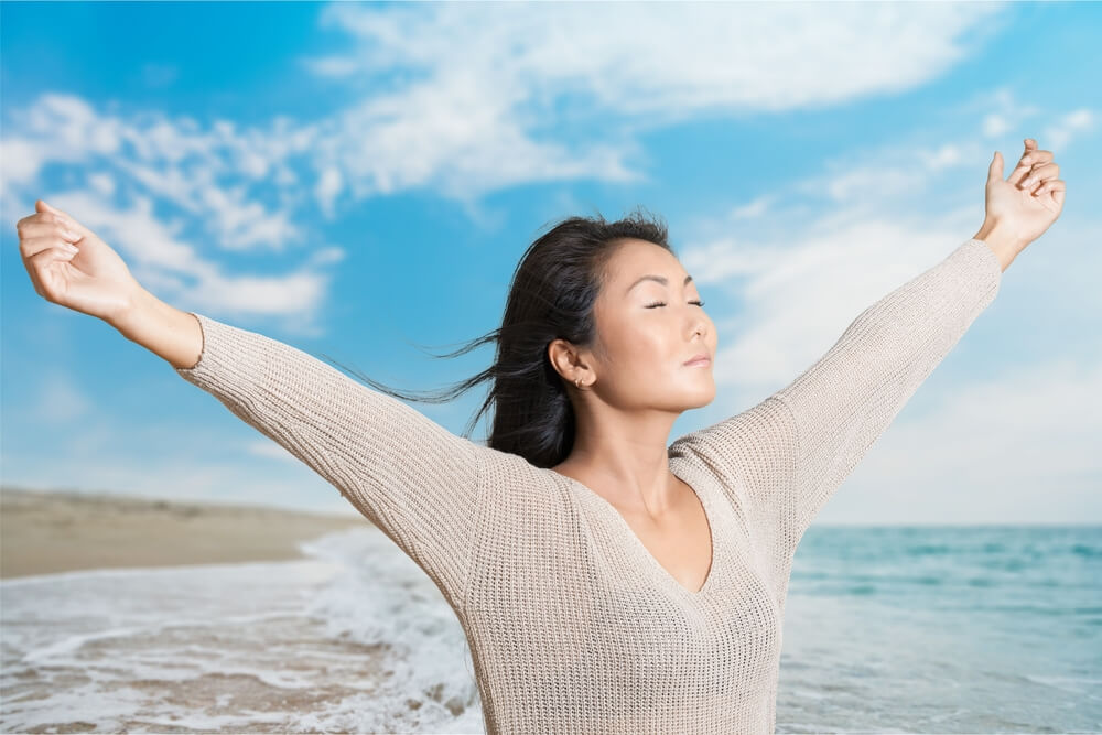 Woman at the beach with arms stretched out enjoying the sun