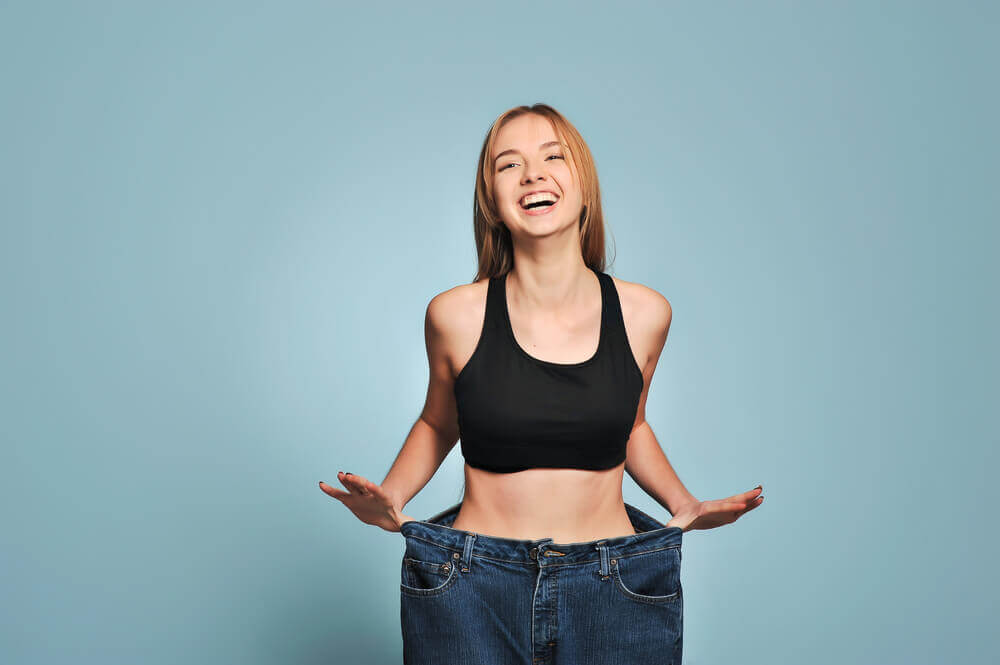Smiling woman placing thumbs in loose-fitting jeans that are too big